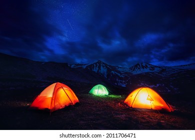 Orange Yellow And Green Gloving Tent At Camping In The Mountain Gorge Under Night Sky With Stars