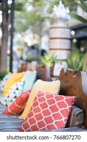 Orange And Yellow Pattern Throw Pillows On An Asians Style Outdoor Patio Chair, With A Blue Striped Cushioned Bench 