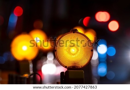 Orange yellow safety lights at road work site. Night time atmosphere on a street in Germany with red and blue  lights. Construction site fenced in to avoid accidents. Symbol for danger and shutdown.