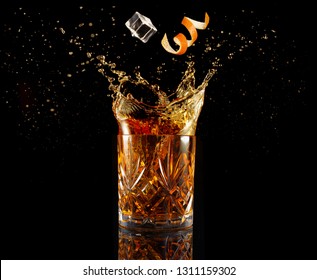 Orange Zest And Ice Falling Into Splashing Cocktail Isolated On Black