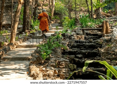 Orange-clad monk walking on a path in the jungle at the Wat Photi Khun Buddhist Monastery near Mae Sot Thailand