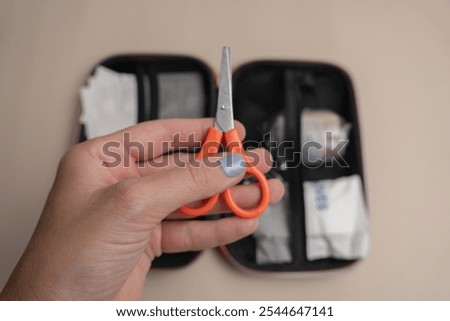 Orange-handled scissors from a first aid kit held in hand, ready for emergency situations