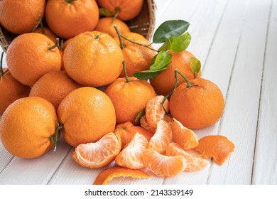 Oranges fruit in the basket with green leaves on the white wood.  Home gardening. Mandarine oranges. Organic tangerines. Orange color. Fresh orange juice. Peeled tangerines.