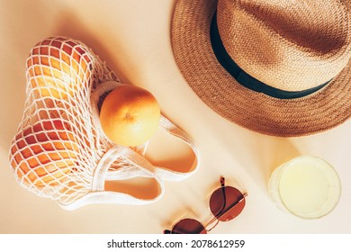 Oranges In A String Bag, Glass With Lemonade, Beach Hat And Sunglasses On Light Background, Top View, Flat Lay