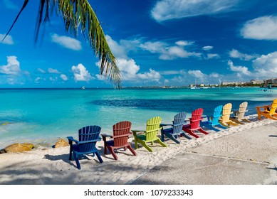 Oranjestad, Aruba - January 15 2018:   Multicolored wooden chairs in the white beach in front of the large luxury hotel on the island of Aruba in the Caribbean Sea