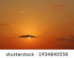 The orb of the sun behind a small cloud in a clear orange sunset sky