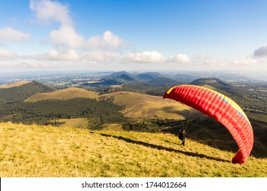 ORCINES, FRANCE - Aug 15, 2018: Man Preparing For Paragliding In Puy De Dome, With The Chaine Des Puys Volcanoes In The Background