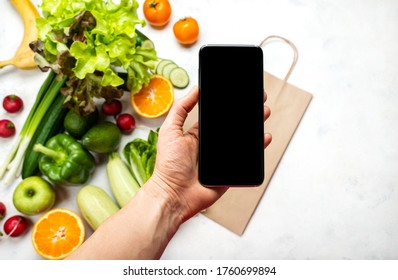 Order, delivery food online. Female hand holding smartphone with blank screen for your text over organic vegetables. Close-up - Powered by Shutterstock