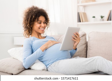 Order kids clothes. Happy pregnant girl using tablet, browsing internet at home