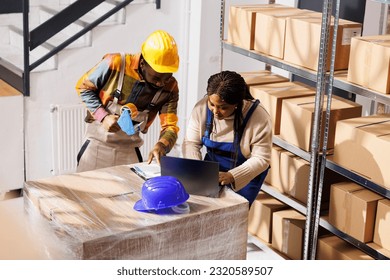 Order pickers team looking at customers list on laptop and clipboard, working in retail storehouse. Ecommerce warehouse african american employees fulfilling customer online purchase