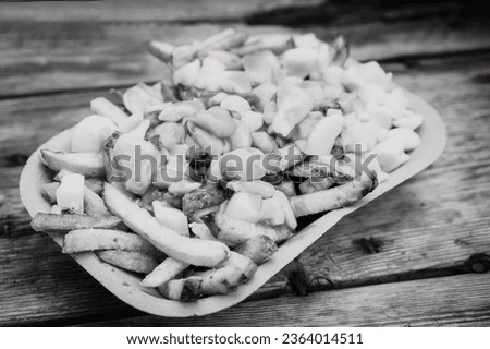 An order of poutine, a French Canadian dish of French fries, gravy, and cheese curds, at a stake street food stand.  Black and white image.