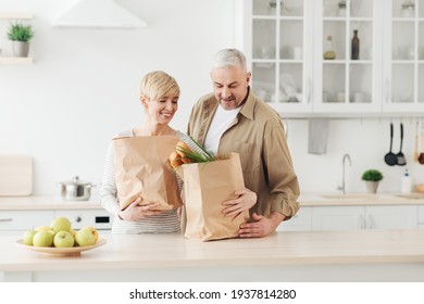 Ordering food online. Senior couple arriving from supermarket with grocery bag and unpacking in kitchen - Powered by Shutterstock