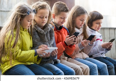 Ordinary Kids Sitting With Mobile Devices In Street