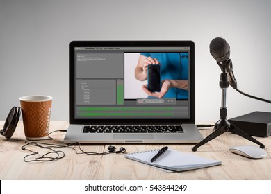 An ordinary workplace of a blogger with a modern laptop and an interface of an application for video editing process. Professional microphone for recording and headphones.