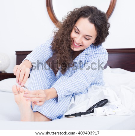 Ordinary young brunette doing domestic pedicure in bedroom 