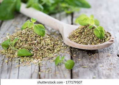Oregano on a wooden spoon (against wooden background)