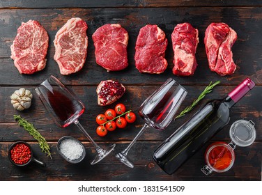 Organic alternative beef cuts top blade steak, chuck roll, rump steak raw beef meat with seasonings, rosemary and butcher cleaver and red wine bottle. Wood textured background. Top view panorama big