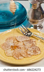 Organic, Baked Johnnycakes With Dripping Warm Maple Syrup  From An Applicator All On A Round, Yellow Plate With A Silver Pitcher And A Stack Of Blue Glass Plates  On A Blue And White Stripped Towel