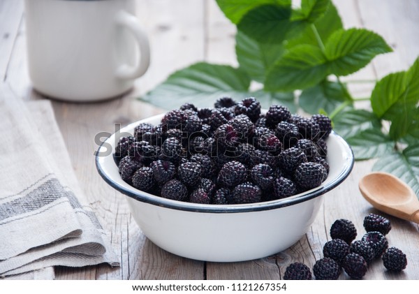 Organic Black raspberry in a white enamel\
plate on a gray wooden\
background