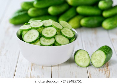 Organic cucumbers slices in a ceramic bowl on a light table, selective focus.