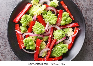 Organic diet fresh salad of romanesco broccoli, bell pepper and red onion sprinkled with sesame seeds close-up in a plate on the table. Horizontal top view from above
