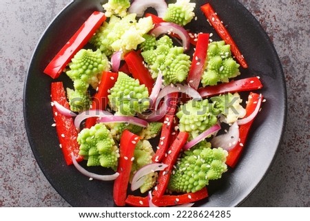 Organic diet fresh salad of romanesco broccoli, bell pepper and red onion sprinkled with sesame seeds close-up in a plate on the table. Horizontal top view from above