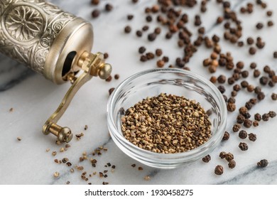 Organic dried Black Peppercorns and coarse ground pepper in a bowl on a marble background close-up. Seasonings and spices. Pepper mill on the table. Selective Focus