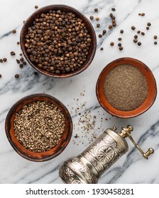 Organic dried Black Peppercorns and peppers are coarse and fine ground in a clay bowls on a marble background close-up. Seasonings and spices. Pepper mill on the table. Selective Focus, top view