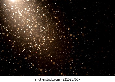 Organic dust particles floating in light ray on black background. Glittering sparkling flickering glowing.