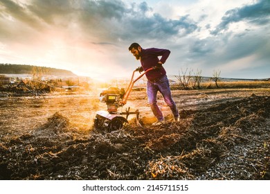organic farming man cultivates the ground at sunset with a tiller  preparing the soil for sowing - Shutterstock ID 2145711515