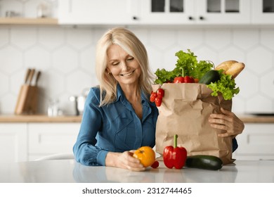 Organic Food Delivery. Happy Mature Lady Unpacking Bag With Groceries In Kitchen Interior, Smiling Elderly Woman Sitting At Table And Holding Fresh Vegetables, Enjoying Healthy Nutrition - Powered by Shutterstock