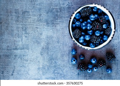 Organic fresh dark berries in vintage mug over rustic background with space for text, top view. Agriculture, Gardening, Harvest Concept.