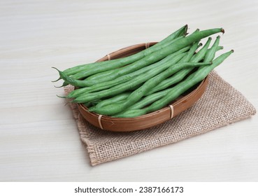 Organic Fresh raw string bean or french beans or Phaseolus vulgaris or common bean on wicker bamboo plate with wooden background.