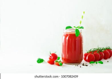 Organic fresh tomato juice in a glass jar, basil, cherry, salt, pepper and straw on light background. Clean eating and diet concept. Copy space