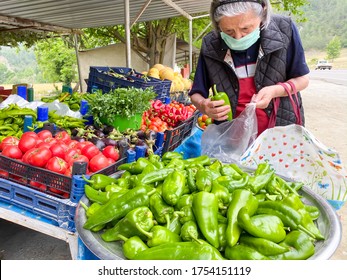 Organic Fruits And Vegetables In Local Organic Farmers Market. Old Woman Buying  Green Pepper At Market. Woman Shopping Wearing A Medical Mask Because Of Coronavirus.