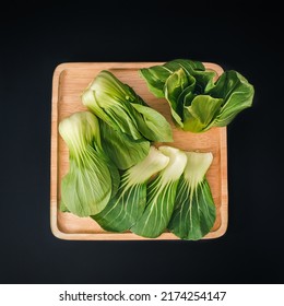 Organic Green Baby Bok Choy Or Brassica Rapa Chinensis On Wooden Plate On Black Background. Popular Chinese Vegetable For Asian Cuisine.Healthy Vegetarian And Vegan Eating.