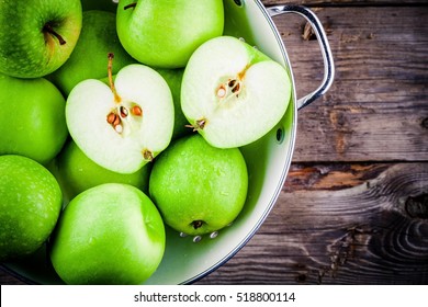 organic green juicy apples in colander on rustic wooden background