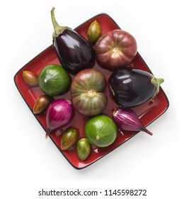 Organic Heirloom Tomatoes, Eggplants, Cupcake Squash, And Sweet Onions On A Red Square Plate, Isolated On White, Top View