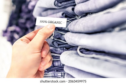 Organic jeans, ethical denim pants. Stack of clothes in store shelf. Label and tag. Sustainable retail fashion and quality product made from natural fabric and textile. Customer buying trousers.