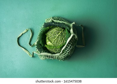 Organic Savoy Cabbage In A Reusable Shopping Bag On Aqua Menthe Table. Fabric Net Bag With Fresh Cabbage. Green Monotone Image With A Single Cabbage.