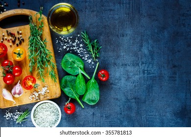 Organic Vegetarian Ingredients, Olive Oil And Seasoning On Rustic Wooden Cutting Board Over Dark Vintage Background With Space For Text, Top View. Healthy Food, Vegan Or Diet Nutrition Concept.