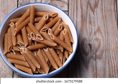 Organic wholemeal pasta close-up. Raw penne rigate on rough wooden background with space for caption.