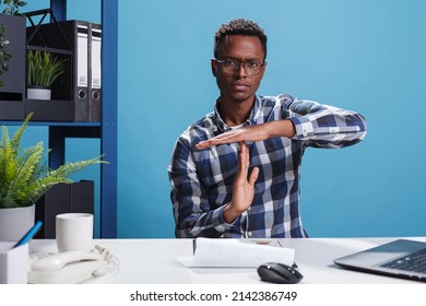 Organization leader gesturing timeout symbol with hands while in office workspace. Marketing company worker making break time sign with arms while sitting at desk in workplace.