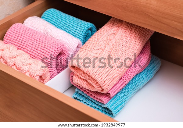 Organization and order.\
A stack of knitted clothes next to a box of neatly folded items in\
a dresser drawer