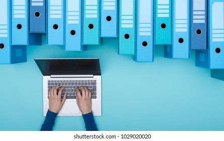 Organisiertes Archiv mit Ringbindern und Frauen, die mithilfe eines Laptops nach Dateien in der Datenbank suchen, Draufsicht