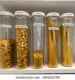 An Organized Pantry Shelf With Various Types Of Pasta In Plastic Containers.