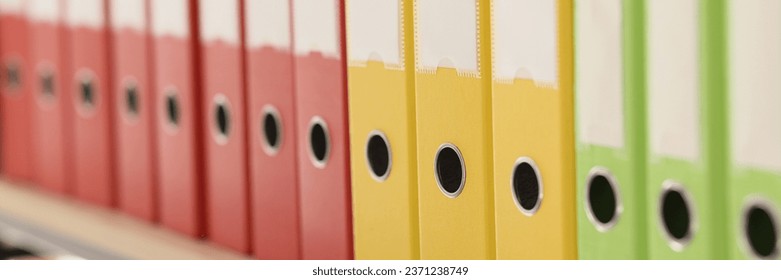 Organized ring binder structure and archive with information. Multi-colored folders with accounting materials put in row on shelf in office closeup