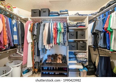 Organized Small Walk In Wardrobe With Clothes And Linen Storage Boxes. Full Walk In Closet With Stacked And Hanging Clothes And A Set Of Shoes Below Near The Laundry Baskets.