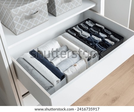 Organized White Wardrobe Drawer with Neatly Folded Clothes and Fabric Boxes, Interior Design Concept of Tidiness and Storage Solutions for Clothing Organization in a Modern Home Setting, Wooden Floor.