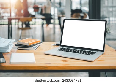 An organized work setup featuring a laptop with a blank screen, notebooks, and a plant on a wooden table in a bright office.